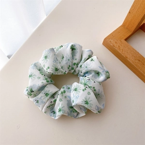 Détail du chouchou en tissu blanc avec des motifs de marguerites bleues et feuilles vertes