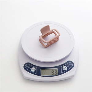 Détail montrant une pince à cheveux carrée rose mat pesant 9,8 g sur une balance digitale