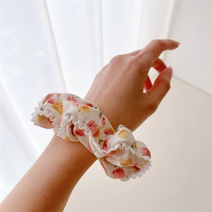 Chouchou fleuri beige avec bordure en dentelle porté au poignet sous lumière douce