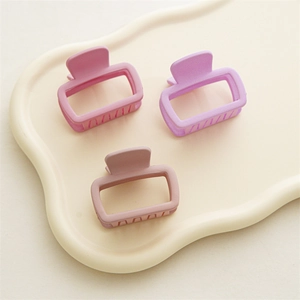 Détail de trois petites pinces à cheveux carrées mates aux tons pastel sur un plateau