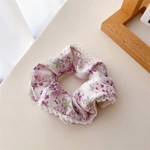 Détail d'un chouchou floral en dentelle avec motifs de fleurs violettes et bordure blanche