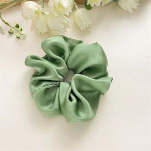 Gros plan sur un chouchou élégant en satin vert avec texture plissée et reflet soyeux