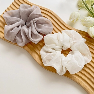 Détail de chouchous en tulle gris-violet et blanc crème sur un plateau en bois avec fleurs