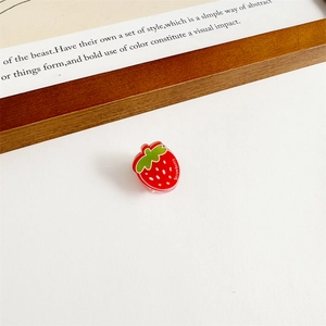 Vue détaillée d'une pince à cheveux fraise rouge avec des pois blancs et des feuilles vertes