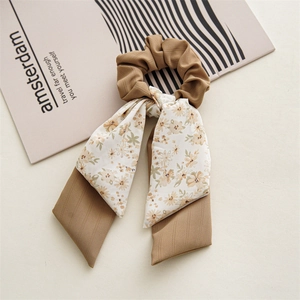 Close-up of floral bow hair scrunchie with long ribbons on minimalist book background