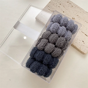 Close-up of thick ribbed towel scrunchies set in clear box with textured stone background