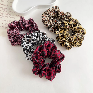Detailed view of four satin leopard print hair scrunchies in red, white, and brown shades