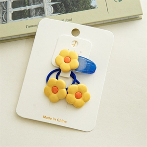 Détail d'une pince à cheveux bleue et d'élastiques avec fleurs jaunes sur carte support