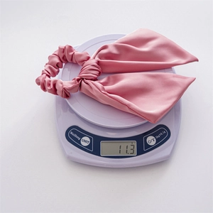 Detailed macro view showing the 11.3g weight of the pink satin bow hair scrunchie