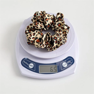Leopard print satin scrunchie weighing 6.5g on a scale, showing elastic hair accessory
