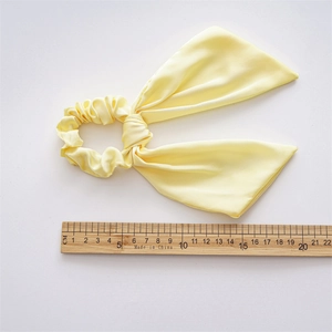 Elegant pale yellow satin scrunchie with long ribbon bow and smooth glossy texture