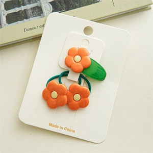Détail de pince à cheveux fleur de frangipanier orange et élastiques sur carte blanche