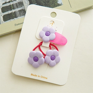 Détail d'une barrette rose et d'un élastique rouge avec fleur violette sur carton