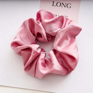 Close-up of elegant pink satin scrunchie with soft fabric folds and silky texture