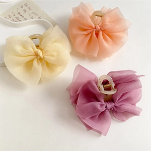 Dettaglio di tre mollette per capelli con fiocco in chiffon nei colori crema, pesca e viola