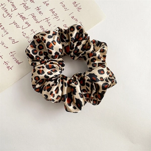 Close-up of leopard print satin scrunchie with silky texture and elegant folds on white background