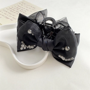 Detail of a large black satin bow hair claw clip with white pearls on a white plate