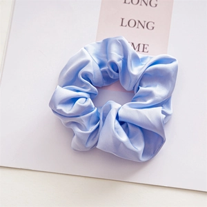 Close-up of light blue satin scrunchie with smooth texture and elegant bow knot detail