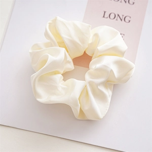 Detailed view of large cream satin scrunchie with silk texture on soft pink backdrop
