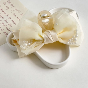 Elegant cream shark hair clip with bow and white pearls on floral ceramic tray
