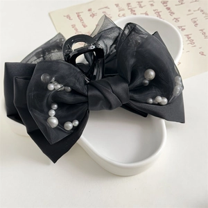 Detail of a large black satin bow hair claw clip with grey pearls on white ceramic tray