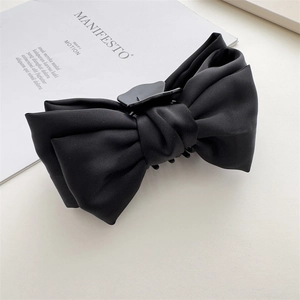 Detail of a large black satin double-layer bow hair claw clip on a minimalist magazine