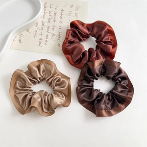 Macro detail of three satin scrunchies in earth tones with elegant ruffled edge texture