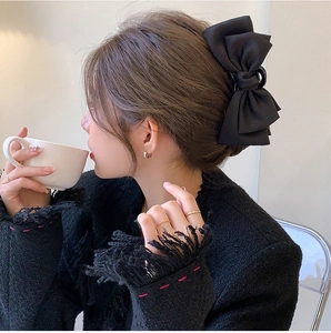 Side view of a large black satin bow hair claw clip worn on a low bun by a model