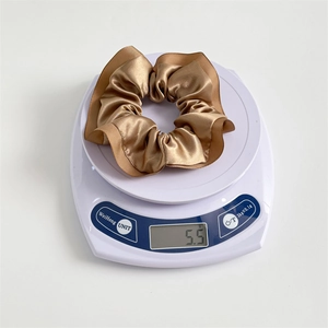 Champagne gold satin scrunchie with ruffle edge, ultra-lightweight design on scale
