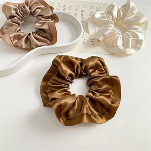 Detailed close-up of three satin scrunchies in cream and brown on a white tray