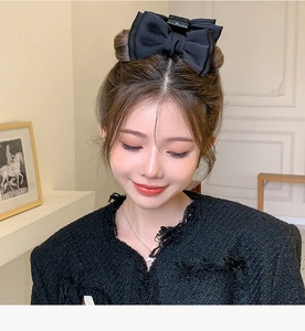 Detail view of a large black satin double bow hair claw clip worn by a model in French style