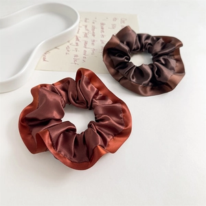 Detail of reddish-brown and dark coffee satin scrunchies with ruffled edges on a tray