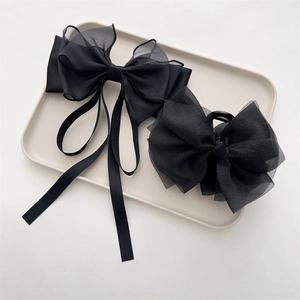 Detail view of large black bow hair clips with organza and satin textures on a tray