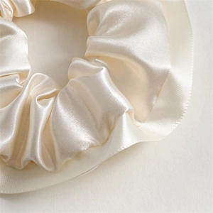 Macro shot of cream satin scrunchie showing pleated silk texture and ribbed edge detail