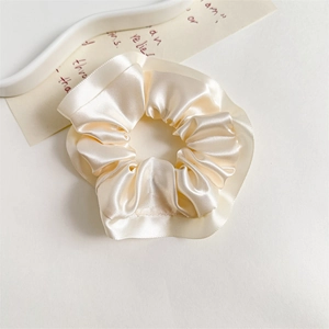 Detailed macro view of the cream satin scrunchie showing glossy texture and ruffle edges