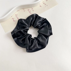 Macro view of silky black satin scrunchie with soft ruffled edges and smooth texture