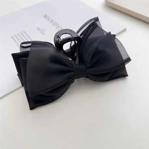 Detail of black bow hair claw clip showing layered satin and mesh texture on light background