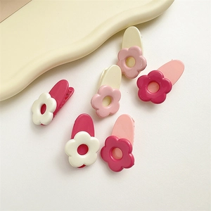 Dettaglio di sei fermagli per capelli a fiore in resina rosa e crema con finitura lucida