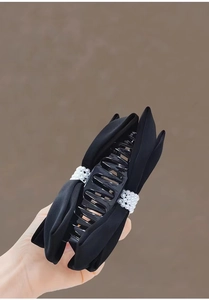 Detail of large black hair claw clip featuring double-sided bows and white faux pearls