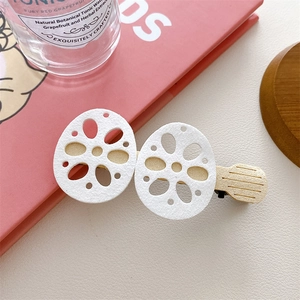 Close-up of white felt lotus root hair clips with a minimalist light wood grain base