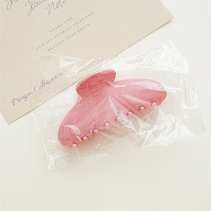 Detailed view of pink hair claw clip in protective packaging with aesthetic background card