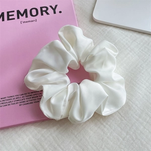 Eleganter weißer Satin-Haargummi mit Faltenstruktur auf einem rosa Buch-Accessoire