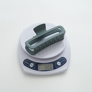 Dark grey-green matte hair claw clip on electronic scale showing 30.6g weight