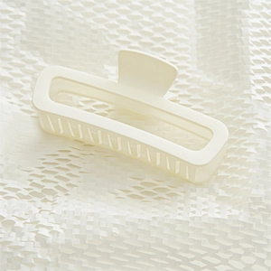 Detail view of a cream matte rectangular hollow hair claw clip on white paper