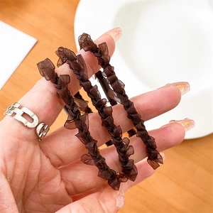 Detail of a brown woven silk hair tie with soft pleated texture held in hand over a desk