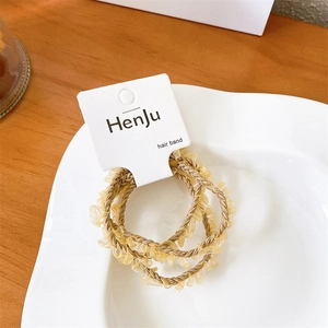 Three-piece champagne gold braided hair bands with lace edges on a ceramic display