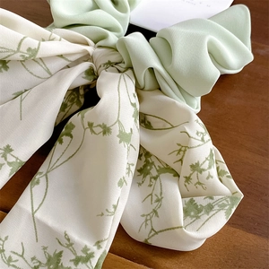 Détail d'un chouchou à nœud floral vert menthe posé sur une surface en bois naturel