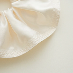Detail of cream silk scrunchie showing fine triple stitching and luxury satin texture