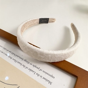Close-up of beige pleated sponge headband featuring a Hand Made label on wooden background