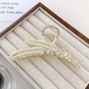 Close-up of golden wheat-shaped hair claw clip with inlaid pearls in a wooden box